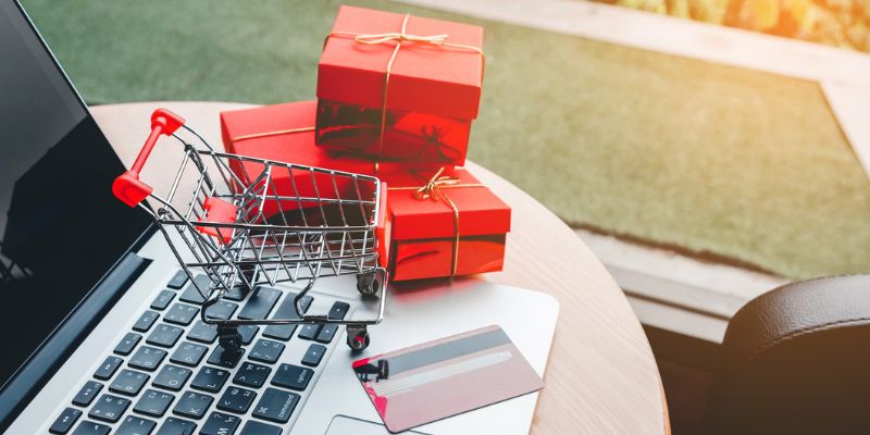 laptop with a minature shopping cart with red presents